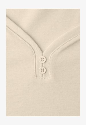 Primer plano de tela beige con escote en V y dos pequeños botones a juego alineados verticalmente en el centro.