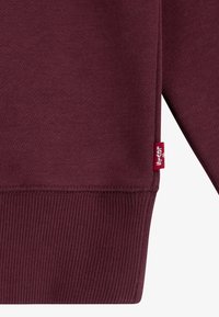 Felpa bordeaux con superficie texturizzata, polsini a costine e orlo laterale. Presenta una piccola etichetta rossa Levi's.