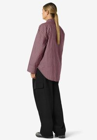 Stripete langermet skjorte i burgunder og krem, med en avslappet passform og høy krage, kombinert med løse svarte cargobukser.