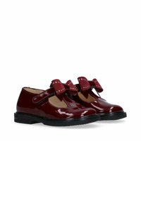 Scarpe in pelle laccata bordeaux lucido con due fiocchi decorativi, caratterizzate da punte arrotondate e suole in gomma nera per una buona aderenza. Includono cinturini in velcro.
