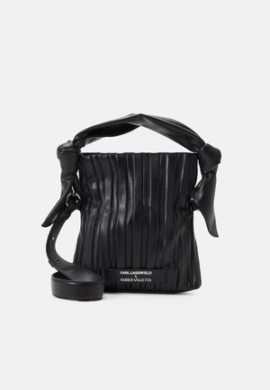 Sac à main en cuir noir avec couture verticale, poignée nouée, bandoulière réglable et étiquette mentionnant Karl Lagerfeld x Amber Valletta.