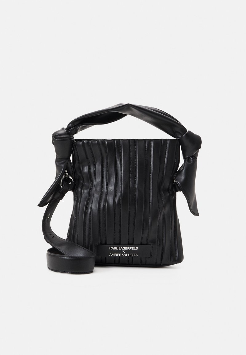 Sac à main en cuir noir avec couture verticale, poignée nouée, bandoulière réglable et étiquette mentionnant Karl Lagerfeld x Amber Valletta.