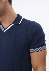 Marineblaues Poloshirt mit kurzen Ärmeln, V-Ausschnitt und weiß gestreiftem Kragen. Enthält strukturierte, vertikale Streifen und gestreifte Bündchen.