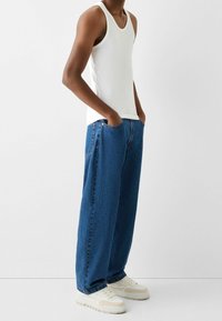 Vit linne, lösa blå denimjeans och vita sneakers. Jeansen har en avslappnad passform med synlig sömnad och sidofickor.