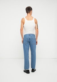 Heledad sinine teksapüksid, lõdva istuvusega, viie tasku disainiga ning peente õmblusdetailidega, kantud koos valge tank topiga ja mustade kingadega.