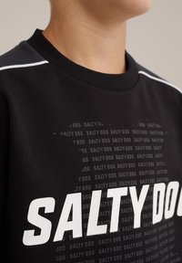 Sweatshirt noir avec "SALTY DOG" en texte blanc gras, tissu texturé, col en rib, et motif de logo subtil sur le corps.