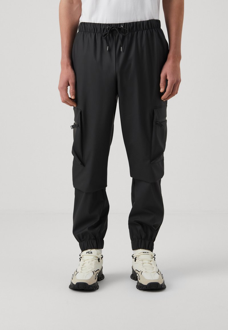 Pantaloni cargo neri con polsini elasticizzati, vita regolabile e molteplici tasche laterali con zip. Il materiale sembra leggero e liscio.