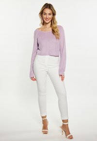 Lila gerippter, verkürzter Pullover mit langen Ärmeln, kombiniert mit weißen, hoch taillierten Skinny Jeans und bandenförmigen, hochhackigen Sandalen.