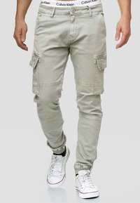 Pantalones cargo de color beige claro con puños elásticos, múltiples bolsillos laterales y una sutil textura descolorida. La cinturilla presenta el logo de Calvin Klein.