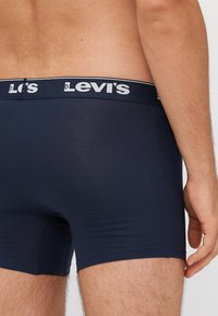 Tengerészkék boxer alsónemű fehér márkázott derékpánttal. Az anyag simának és testhezállónak tűnik, a varrás pedig a lábnyílásokat körvonalazza.