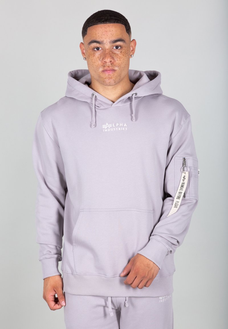 Svetlo šedá mikina s kapucňou vyrobená z mäkkej látky, s prednou vreckom, kapucňou na šnúrku a s logom na hrudi a na rukáve.