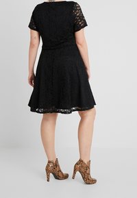 Svart spetsklänning med korta ärmar, åtsittande midja och utsvängd kjol. Kombinerad med strukturerade bruna och svarta hälar med ormskinnsmönster.