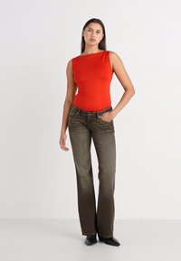 Red, one-shoulder bodysuit paired with olive green, flared jeans. The jeans feature front pockets and a slight sheen, finished with black shoes.