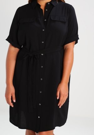 Musta napillinen mekko pehmeästä kankaasta, jossa on käännetyt hihnat, kaksi rintataskua, vyö vyötäröllä ja kaareva helma.