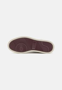 Schuhsohle mit einem gemusterten burgunderfarbigen Gummiboden, der kreisförmige und wellenartige Rillen aufweist, umrandet von einem cremefarbenen Rand.