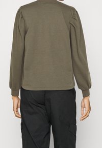Top de manga larga verde oliva con hombros abullonados, escote redondeado y puños acanalados, combinado con pantalones cargo negros con bolsillos laterales.