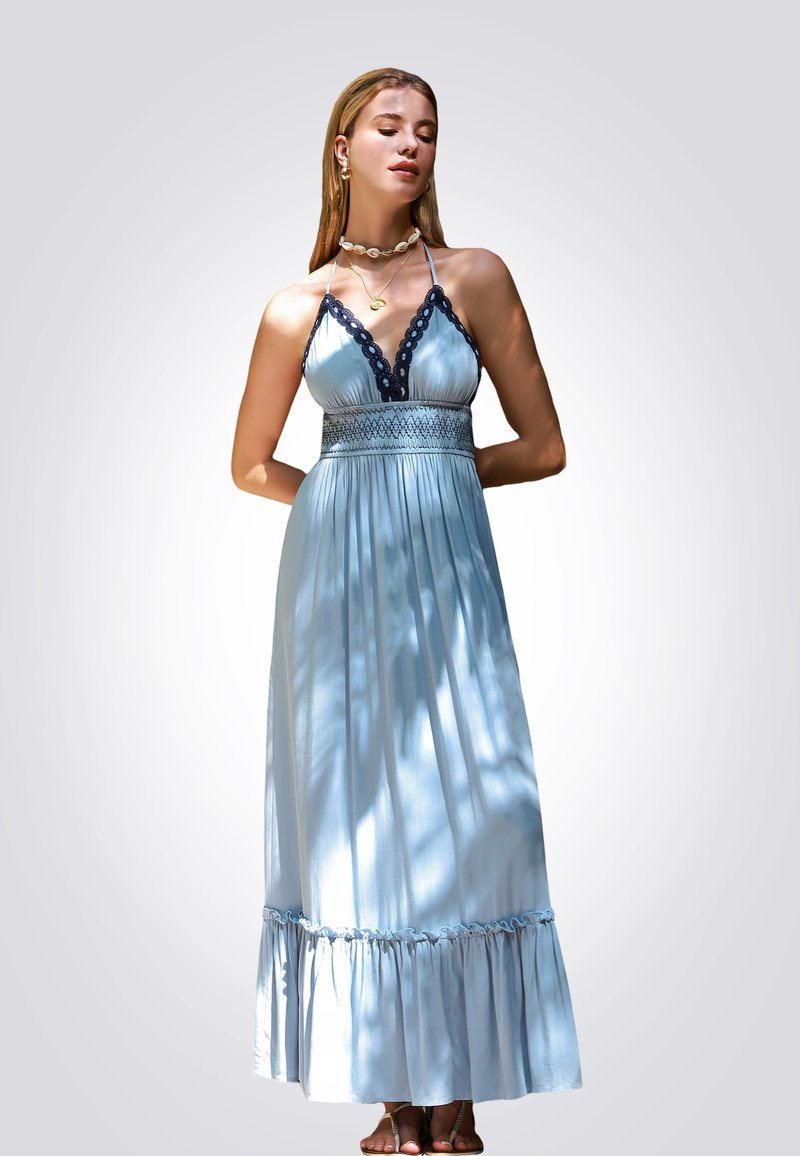 Robe maxi bleu clair avec un col halter, garniture en dentelle marine, corsage smocké et ourlet à volants. Portée avec des sandales douces et des colliers superposés.