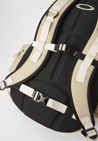 Rucksack mit schwarzen gepolsterten Abschnitten und beige-farbenen Stoffakzenten, verstellbaren Trägern und Clip-Hardware zur Sicherung des Inhalts.