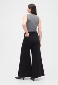 Calças pretas de ganga com pernas largas, cintura alta e bolsos traseiros destacados. Combinadas com um top cinzento ajustado sem mangas.