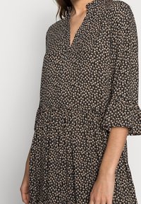 Svart klänning med ett subtilt blommönster i beige, med V-ringning, tre fjärdedels ärmar och en utsvängd nederkant.