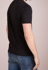 Camiseta negra de cuello redondo, manga corta, fabricada en algodón suave, de corte ajustado, combinada con jeans de mezclilla azul oscuro. Diseño minimalista, sin detalles notables.