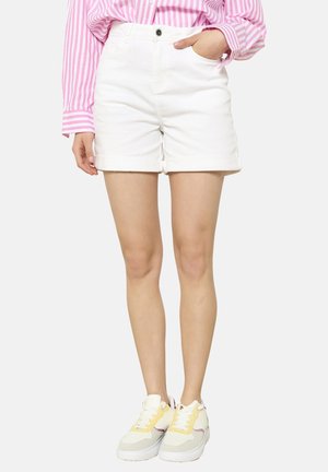 Weiße Jeansshorts mit umgeschlagenem Saum, kombiniert mit mehrfarbigen Sneakers mit gelben Akzenten und einem pink gestreiften Langarmshirt.