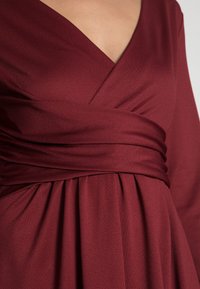 Burgundia värvi ümar kaelusega mähis Kleid, millel on pikad varrukad, volditud seelik ja lai vöökoht. Valmistatud tekstuurilisest, voolavast kangast.