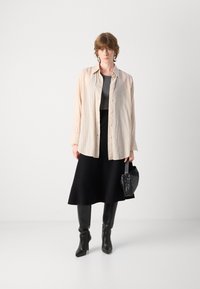Light beige button-up shirt, gray top, black skirt, and knee-high black boots. Accented with a small black handbag. Smooth textures throughout.