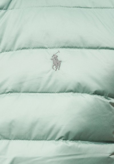 Ανοιχτό πράσινο μπουφάν φουσκωτό με ραφές. Διαθέτει κεντημένο γκρι λογότυπο στο στήθος. Απαλή, λεία υφή.