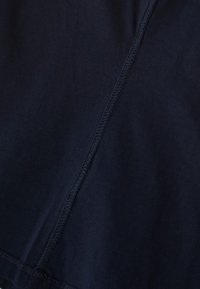 Námorně modrý bavlněný textil s hladkým povrchem a viditelným švem podél švu, což vytváří čistý a jednoduchý design.