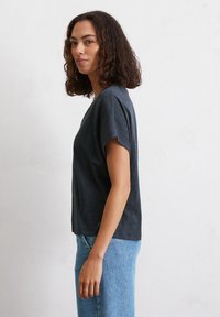 Maglietta corta nera con maniche corte e vestibilità ampia, realizzata in tessuto morbido, abbinata a jeans in denim azzurro chiaro. Design semplice senza motivi.
