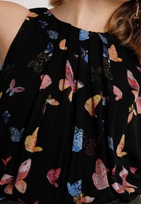 Blusa nera con stampe di farfalle colorate in diverse tonalità. Il design plissettato aggiunge texture. Senza maniche con scollatura rotonda.