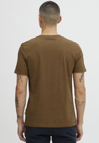 Brun kortermet t-skjorte med rund hals, laget av mykt stoff. Har minimalistisk logo på baksiden. Glatt tekstur.