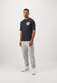 Navy t-shirt with graphic print, gray cargo sweatpants, and white sneakers. Casual fit, short sleeves, and lightweight fabric.