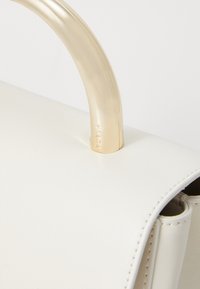 Borsa a mano in pelle bianca con una superficie liscia, dotata di una maniglia in metallo dorato elegante e di un discreto logo impresso sul lato.