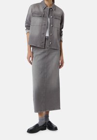 Graue Jeansjacke mit zwei Brusttaschen, kombiniert mit einem passenden grauen Maxirock. Schwarze Loafers und graue gerippte Socken vervollständigen das Outfit.