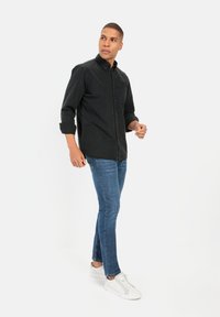 Czarna koszula z guzikami, z możliwością podwinięcia rękawów, zestawiona z niebieskimi spodniami typu slim-fit i białymi sneakerami. Prosty i nowoczesny design.