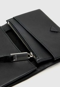 Saco de couro preto com uma textura suave, apresentando um compartimento com fecho e uma alça para transporte. Inclui um detalhe em forma de triângulo.