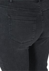 Jean en denim noir en gros plan montrant une unique poche arrière et des passants de ceinture sur un vêtement ajusté.