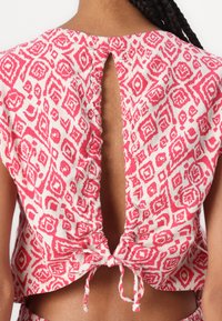 Cotton top with a pink and white geometric pattern, features a back opening with a tie detail, and a soft, textured finish.