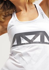 Débardeur de sport blanc avec un design en maille respirante, des accents géométriques noirs distinctifs et un logo Reebok en haut à gauche.