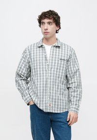 Καρό πουκάμισο με κουμπιά σε λευκούς, πράσινους και μαύρους τόνους. Διαθέτει γιακά, μακριά μανίκια και κεντημένο λογότυπο στο στήθος.