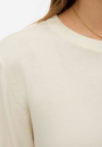 Pull en maille texturée couleur crème avec un col côtelé et des manches courtes, présentant une finition de tissu lisse et douce.