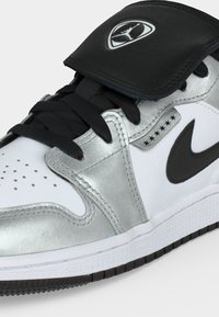Λευκό και μεταλλικό ασημί Nike Air Jordan αθλητικό παπούτσι με μαύρα κορδόνια, μαύρο swoosh και δερμάτινο πτερύγιο με το λογότυπο Jumpman.