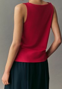 Haut rouge sans manches avec une finition lisse et un col rond, associé à une jupe noire. Le tissu semble léger et tombe élégamment.