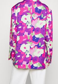 Chaqueta con estampado floral en tonos vibrantes de rosa, púrpura y verde. Corte holgado con mangas largas y cuello clásico. Textura de tela suave.