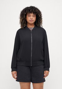 Black bomber jacket with a smooth texture, zip closure, ribbed cuffs and hem, and relaxed fit, paired with dark denim shorts.