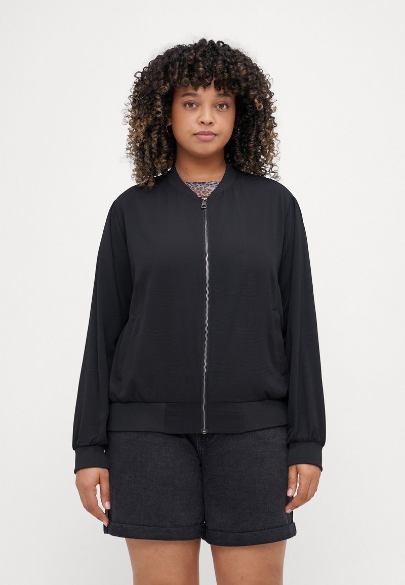 Black bomber jacket with a smooth texture, zip closure, ribbed cuffs and hem, and relaxed fit, paired with dark denim shorts.
