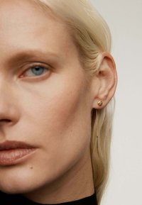 Pendientes de oro con un pequeño stud en la parte superior y una cadena larga y delgada con un colgante recto que cuelga hacia abajo. Acabado suave, diseño minimalista.