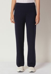 Marinblå, vida svettbyxor med mjuk textur, elastisk midja och inga synliga mönster. Bärs med vita sneakers.